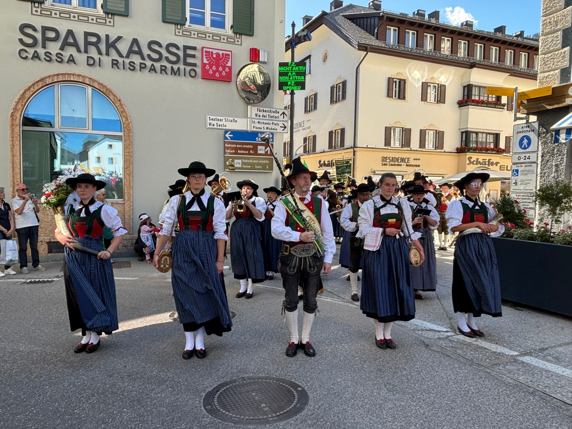 A traditional Tyrolean brass band in dirndls and lederhosen standing at attention in a mountain town square