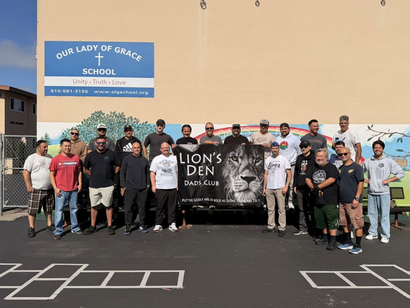 The Lion's Den Dads Club gathered with their banner outside the school