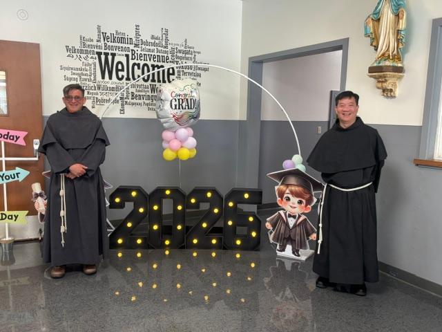 Two staff members beside a 2026 grad cutout and a Welcome word cloud