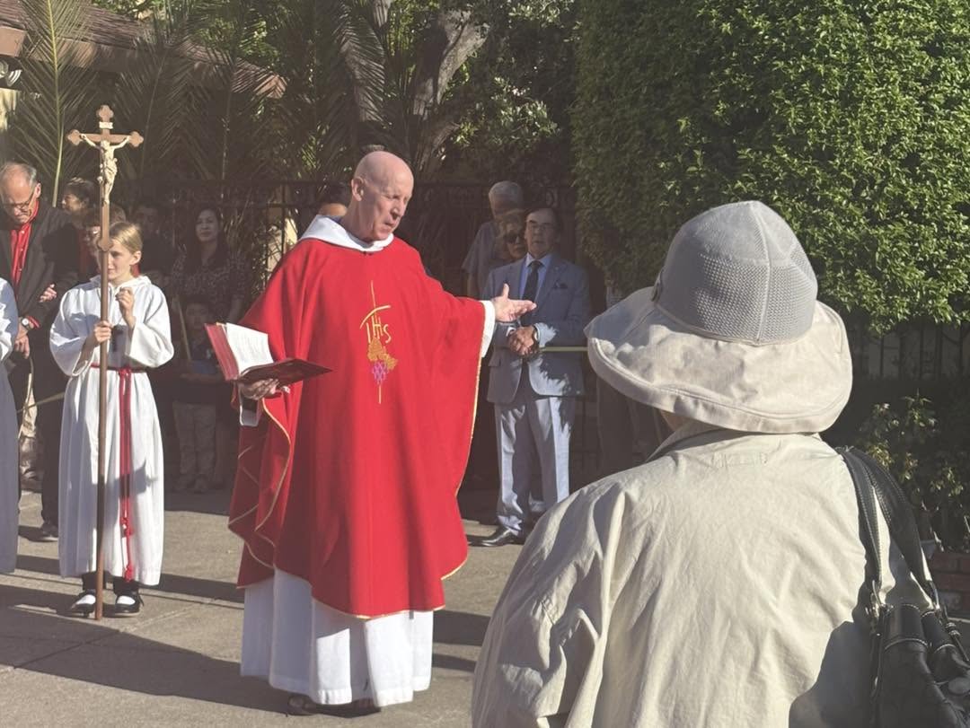 Father Tom in red vestments greeting parishioners outside the church