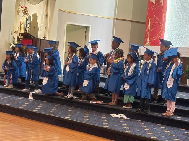 Kindergarten graduates in blue caps and gowns on the steps of the church